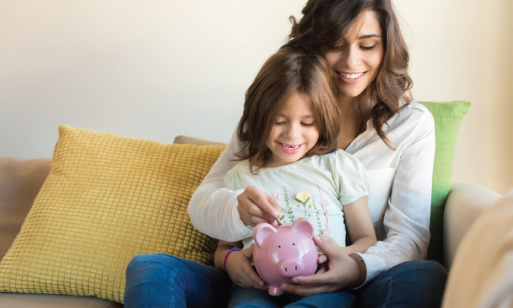 Mother and daughter putting money in piggy bank